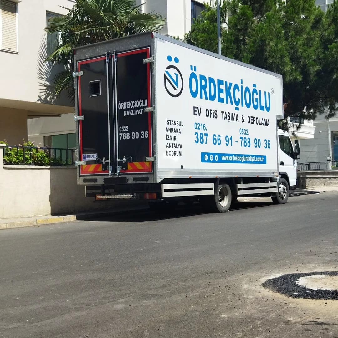 Ördekçioğlu kapalı kasa kamyonunun yan ve arka görünümü; kasada “Ev Ofis Taşıma & Depolama” yazısı, şehir adları ve telefon numaraları.